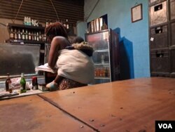 Bartender selling liquor with child strapped on her back