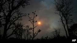FILE - The sun sets behind the smoke of large-scale fires in the native Cerrado forest at the National Park in Brasilia, Brazil, Sept. 5, 2022.