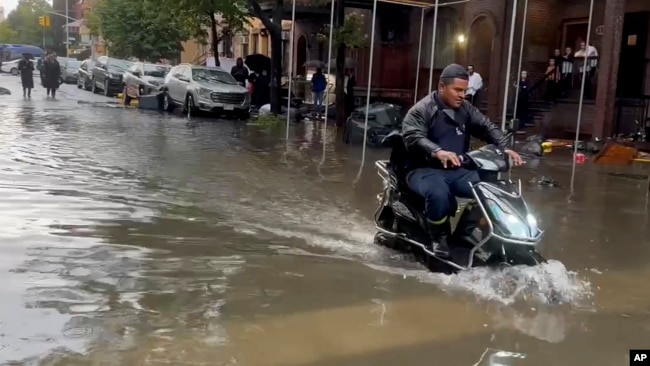 In this photo taken from video, a man drives a scooter through flood waters, Sept. 29, 2023, in the Brooklyn borough of New York.