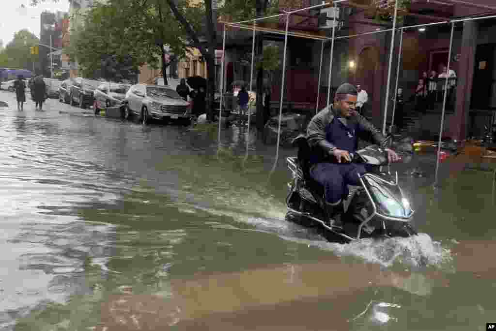 Nesta fotografia tirada de um vídeo, um homem conduz uma moto pelas águas das cheias, a 29 de setembro de 2023, no bairro de Brooklyn, em Nova Iorque.
