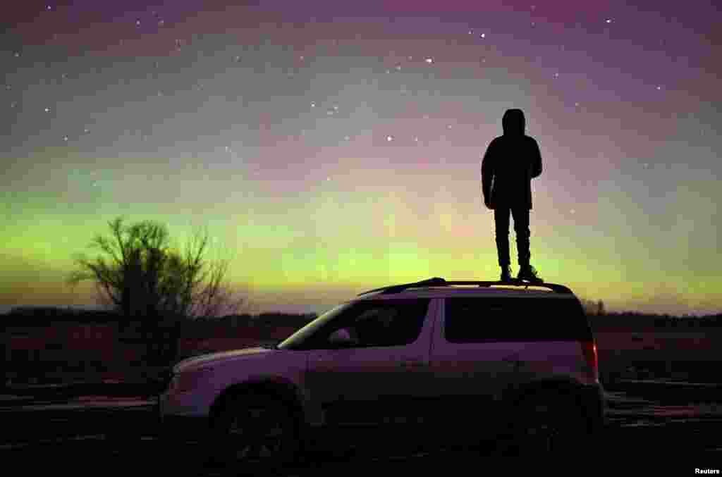 A person stands on a car while looking at Auroras, caused by a coronal mass ejection on the sun, that illuminate the skies in the southwestern Siberian Omsk region, Russia.