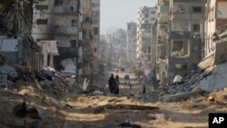 Palestinians walk between the remains of destroyed buildings following the Israeli bombardment on the main road of Gaza City on Jan. 2, 2024.