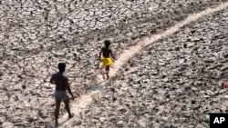 FILE - A man and a boy walk across the dried bed of the Yamuna River in New Delhi, India, May 2, 2022. In an annual climate report, the World Meteorological Organization said Nov. 2, 2023, that the climate crisis was generating a global health crisis.