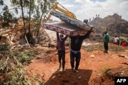 Dua pria membawa kasur setelah tempat pembuangan sampah runtuh di Kampala pada 10 Agustus 2024. (Foto: AFP)