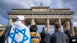 Varias personas, una envuelta en una bandera israelí, participan en una manifestación contra el antisemitismo frente a la Puerta de Brandeburgo, en Berlín, Alemania, el 22 de octubre de 2023.