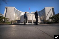 FILE - Pedestrians wearing face masks walk past the People's Bank of China in Beijing on March 3, 2023.