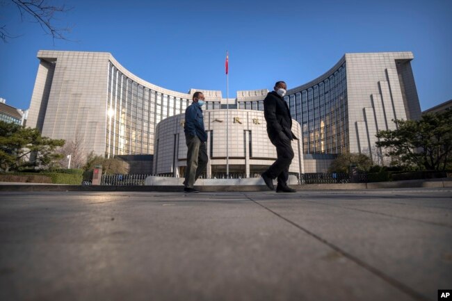 FILE - Pedestrians wearing face masks walk past the People's Bank of China in Beijing on March 3, 2023.