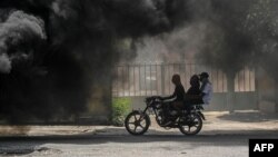 Bodaboda ikipita pembeni mwa moshi uliotokana na mataili yaliyochomwa moto huko Port-au-Prince Agosti14, 2023. Picha na Richard PIERRIN / AFP.