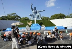 Sejumlah pengunjung di Taman Perdamaian (Peace Park) merunduk setelah alarm gempa bumi dibunyikan di Nagasaki, bagian barat Jepang, Kamis, 8 Agustus 2024. (Foto: Kyodo News via AP)