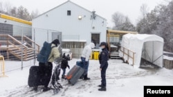 FILE - A family crosses into Canada at Roxham Road, an unofficial crossing point from New York state to Quebec for asylum-seekers, in Champlain, N.Y., March 25, 2023. 