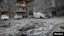 Para penghuni dekat gedung apartemen dan kendaraan-kendaraan yang rusak dalam serangan misil di tengah invasi Rusia ke Ukraina, di Kharkiv, Ukraina, 8 Desember 2023. (Foto: Vyacheslav Madiyevskyy/Reuters)