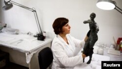 FILE - Restorer Laura Rivaroli works on a bronze statue of Apollo in the pose of an archer. It was discovered in the muddy ruins of an ancient spa in San Casciano dei Bagni, a hilltop village in southern Tuscany. May 29, 2023. (REUTERS/Guglielmo Mangiapane)