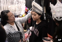 Alesia Lor tries on traditional Hmong New Year headwear with family members at a stall in the Hmong Village covered market in St. Paul, Minnesota, Nov. 16, 2023.