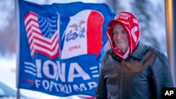 资料照片：艾奥瓦州厄本代尔一名男子站在一面写着“艾奥瓦支持特朗普”的旗帜旁。（2024年1月14日）