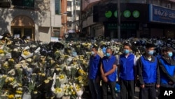 Security personnel in blue vests stand guard in front of the flowers laid by residents near a residential building where the late Chinese Premier Li Keqiang spent his childhood in Hefei city, in central China's Anhui province, Nov. 2, 2023. 