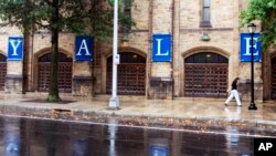 FILE - A woman walks by a Yale sign reflected in the rainwater on the Yale University campus in New Haven, Conn., Aug. 22, 2021. 