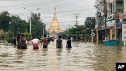 ইয়াংগনের প্রায় ৮০ কিলোমিটার (৫০ মাইল) উত্তর-পূর্বে বাগো-র শুই মাও তাও প্যাগোডার কাছে জলমগ্ন রাস্তা পেরিয়ে চলেছেন স্থানীয় বাসিন্দারা। ৯ অক্টোবর, ২০২৩।