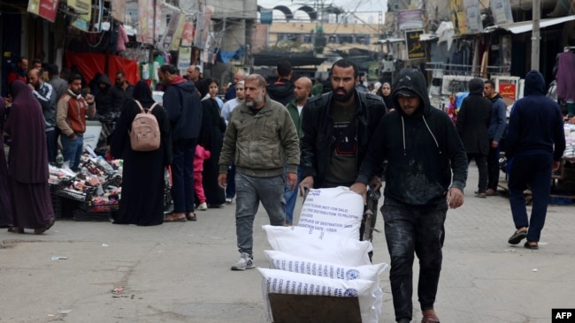 FILE - Displaced Palestinians push a barrow loaded with bags of flour they received from the U.N. Relief and Works Agency for Palestine Refugees in Rafah in the southern Gaza Strip, Jan. 28, 2024,