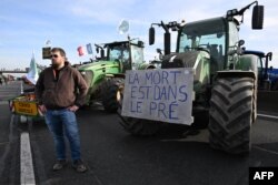 Seorang petani Prancis ikut serta dalam aksi protes pemblokiran jalan di jalan raya A4 di samping traktor dengan plakat bertuliskan "Kematian ada di ladang" dekat Jossigny, timur Paris, 29 Januari 2024. (Bertrand GUAY / AFP)