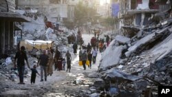 FILE - Palestinians walk through a dark streak of sewage flowing into the streets of the southern town of Khan Younis, Gaza Strip, on July 4, 2024.