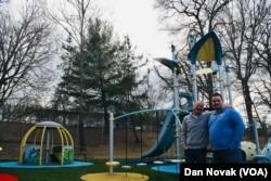 Mark Rapaport, left, and Dan Hack in front of the playground at Transformation Academy. The We-Go-Round on the left has a special spot for kids with wheelchairs. (Dan Novak/VOA)