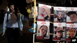 FILE - A member of Israeli security forces looks at posters of children held hostage by Hamas in the Gaza Strip, in Tel Aviv, Israel, Nov. 23, 2023.