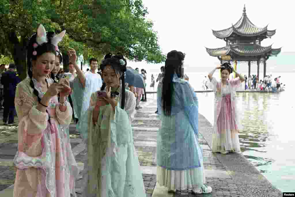 Women wearing traditional dresses look at their cell phones at West Lake during the first day of the holidays due to the Mid-Autumn Festival and National Day in Hangzhou, China.