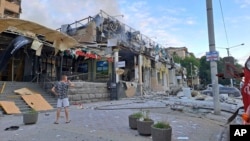 FILE - In this photo provided by the Ukrainian Donetsk Regional Administration, a man stands on a street in front of a shop and restaurant RIA Pizza destroyed by a Russian attack in Kramatorsk, Ukraine, June 27, 2023.