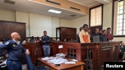 A police officer looks on as suspects stand in the dock during a court appearance in connection with an 18-year-old student who was allegedly kidnapped after engaging with someone on Grindr app, at the Johannesburg Magistrates Court in South Africa on November 15, 2023.