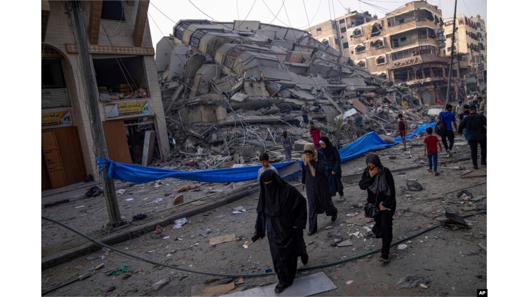 Warga Palestina berjalan di dekat reruntuhan sebuah bangunan setelah terkena serangan udara Israel, di Kota Gaza, 8 Oktober 2023. (Foto: AP)