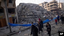 Palestinians walk by the rubble of a building after it was hit by an Israeli airstrike, in Gaza City, Oct. 8, 2023. 
