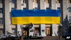 Općinski radnici ukrašavaju zid zgrade regionalne uprave ogromnom nacionalnom zastavom kako bi obilježili godinu dana otkako su ukrajinske trupe očistile grad od ruske vojske, u Khersonu, Ukrajina, 10. studenog 2023.