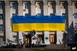 Para pekerja kota menghiasi dinding gedung pemerintahan daerah dengan bendera nasional berukuran besar di Kherson, Ukraina, 10 November 2023. (Foto: AP)