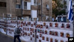 A man passes by a fence with photographs of hostages, mostly Israeli civilians who were abducted during the Oct. 7, unprecedented Hamas attack on Israel, in Ramat Gan, Israel, Nov. 22, 2023.