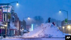 People stand on an large snow pile in Oskaloosa, Iowa, Jan. 9, 2024.