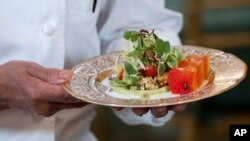 A chef holds the first course, a marinated millet and grilled corn kernel salad with compressed watermelon and a tangy avocado sauce during a media preview, June 21, 2023, at the White House.