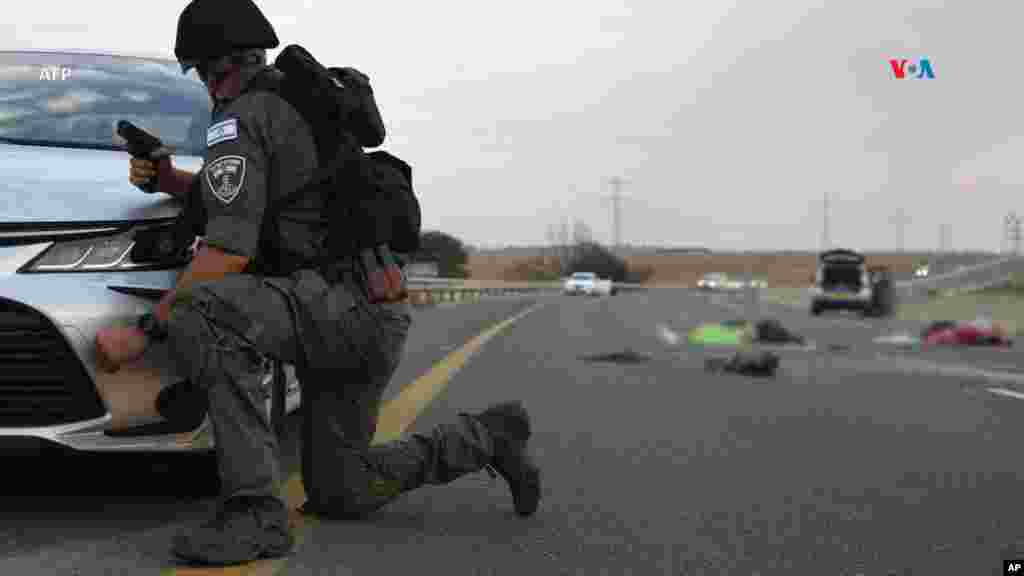 Un soldado israelí se protege tras un automóvil mientras custodia dos cadáveres en una carretera principal cerca del kibutz Gevim, por la frontera con Gaza.