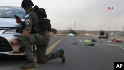 Un soldado israelí se esconde detrás de un automóvil mientras custodia dos cadáveres en una carretera principal cerca del Kibbutz Gevim, a lo largo de la frontera con Gaza.