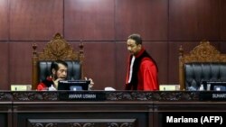 Hakim Mahkamah Konstitusi Anwar Usman (kiri) dan Suhartoyo (kanan) berbincang saat sidang memutus permohonan perubahan syarat pencalonan presiden, di Jakarta, 16 Oktober 2023. (Foto: AFP/MARIANA)