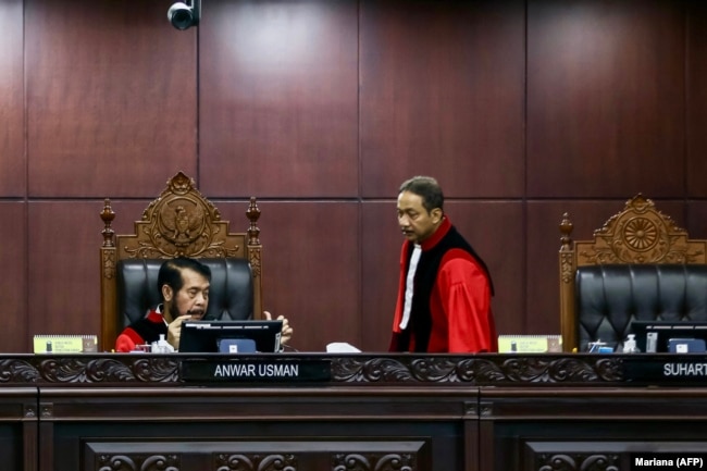 Hakim Mahkamah Konstitusi Anwar Usman (kiri) dan Suhartoyo (kanan) berbincang saat sidang memutus permohonan perubahan syarat pencalonan presiden, di Jakarta, 16 Oktober 2023. (Foto: AFP/MARIANA)