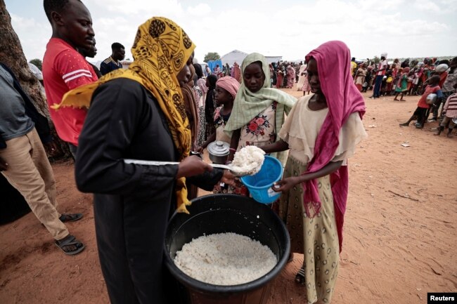 Sudanese people who fled the conflict in Geneina in Sudan's Darfur region, receive rice portions from Red Cross volunteers in Ourang on the outskirts of Adre, Chad, July 25, 2023.