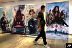 Seorang pria mengenakan masker, berjalan melewati poster film Disney "Mulan" di sebuah bioskop di Beijing, China, 11 September 2020. (AP/Mark Schiefelbein)