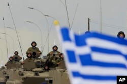 Cyprus' soldiers on the military vehicles pass behind a Greek flag during a military parade marking the 63th anniversary of Cyprus' independence from British colonial rule, in divided capital Nicosia, Cyprus, Oct. 1 2023.