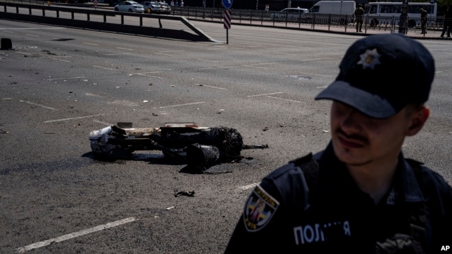 Un oficial de policía ucraniano protege un fragmento del cohete después de un ataque con cohetes rusos en Kiev, Ucrania, el lunes 29 de mayo de 2023.