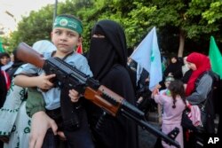 A supporter of the Islamist Hamas movement carries her son, who holds a toy machine gun, during a protest in the southern port city of Sidon, Lebanon, July 31, 2024, to condemn the killing of Hamas political chief Ismail Haniyeh.