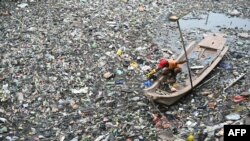 Seorang petugas kebersihan berusaha membersihkan sampah plastik yang mengotori saluran air di Kanal Buckhingham di Chennai, India, pada 16 November 2023. (Foto: AFP/R. Satish Babu)