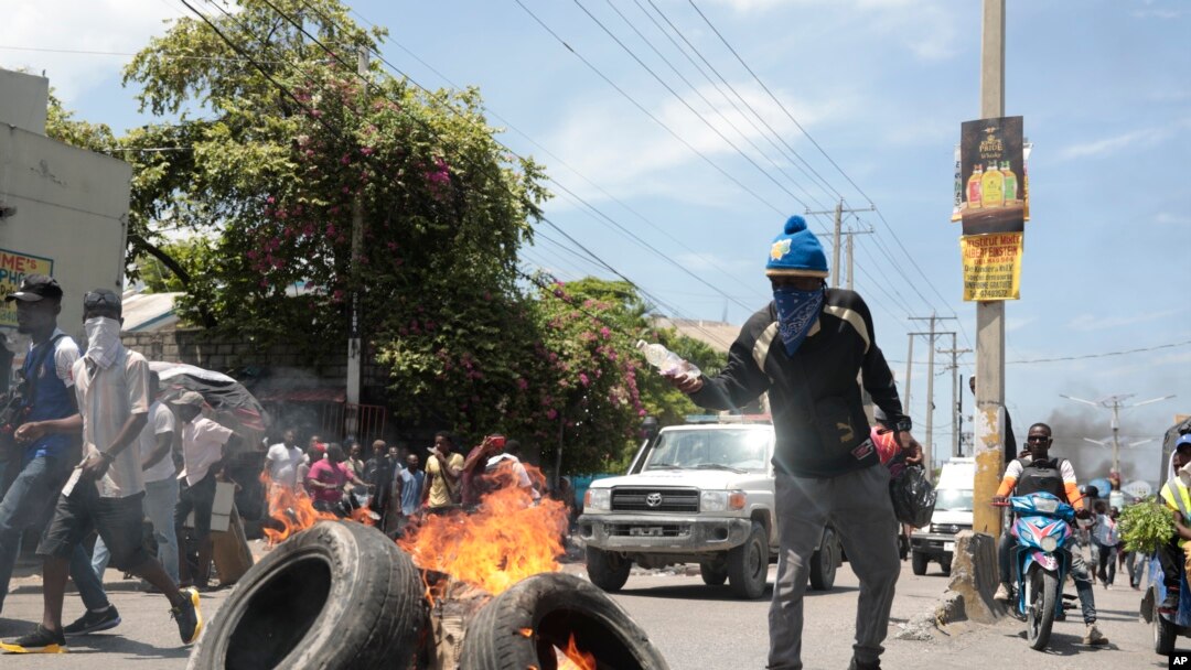 Seorang demonstran menyiramkan bensin ke arah ban yang terbakar dalam aksi protes menentang meningkatnya ketidakamanan di Haiti. Protes berlangsung di Port-au-Prince, Haiti, pada 17 September 2023. (Foto: AP/Odelyn Joseph)