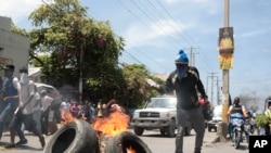 FILE - A protester adds fuel to burning tires during a protest against insecurity in Port-au-Prince, Haiti, Sept. 17, 2023.
