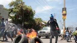 Seorang demonstran menyiramkan bensin ke arah ban yang terbakar dalam aksi protes menentang meningkatnya ketidakamanan di Haiti. Protes berlangsung di Port-au-Prince, Haiti, pada 17 September 2023. (Foto: AP/Odelyn Joseph)