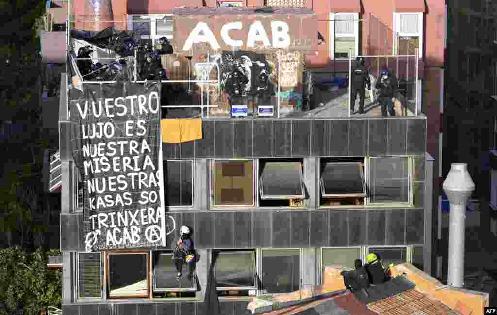 An occupant of the illegally occupied El Kubo squat-house hangs from a rope next to a banner as members of the police force carry out a forced vacating of the building, in Barcelona, Spain.